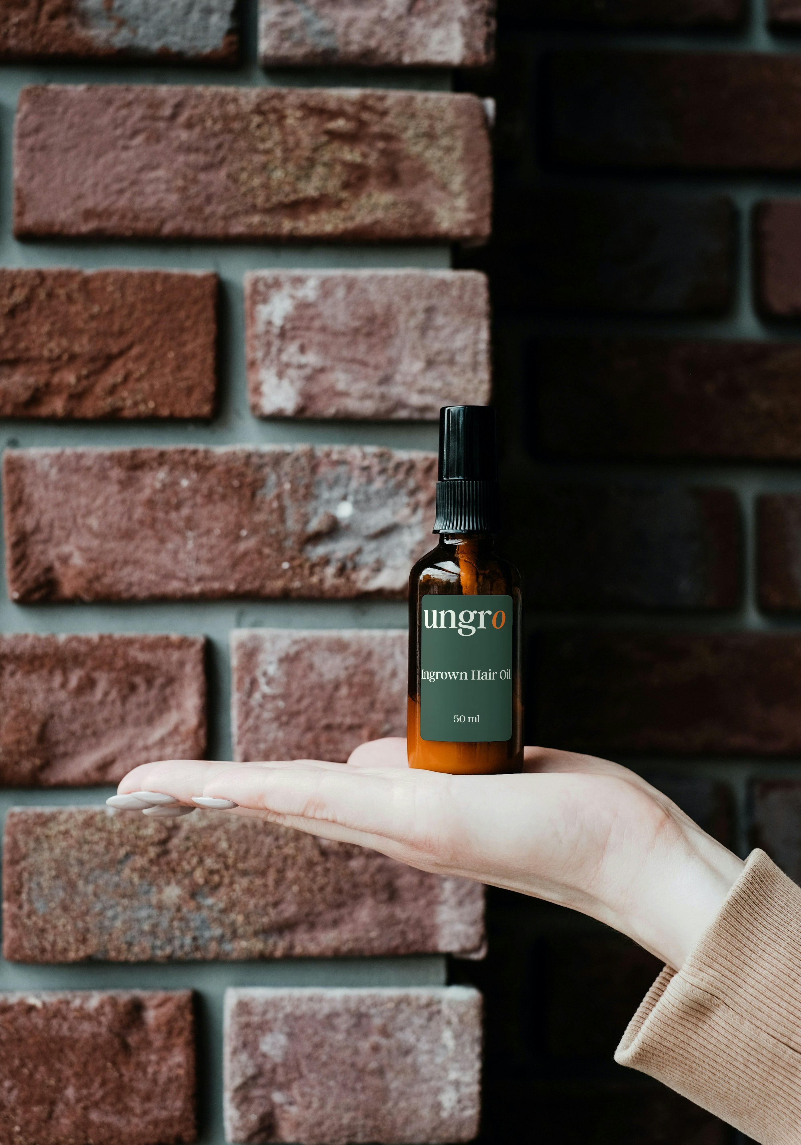 ungro Ingrown Hair Oil, 50 ml amber glass bottle resting on an open palm against a brick wall